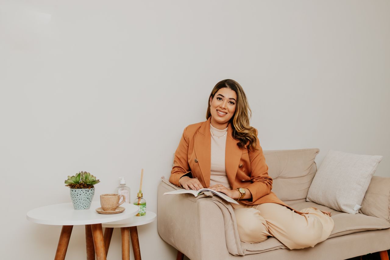 A woman in a stylish outfit reading on a cozy sofa with a table nearby.