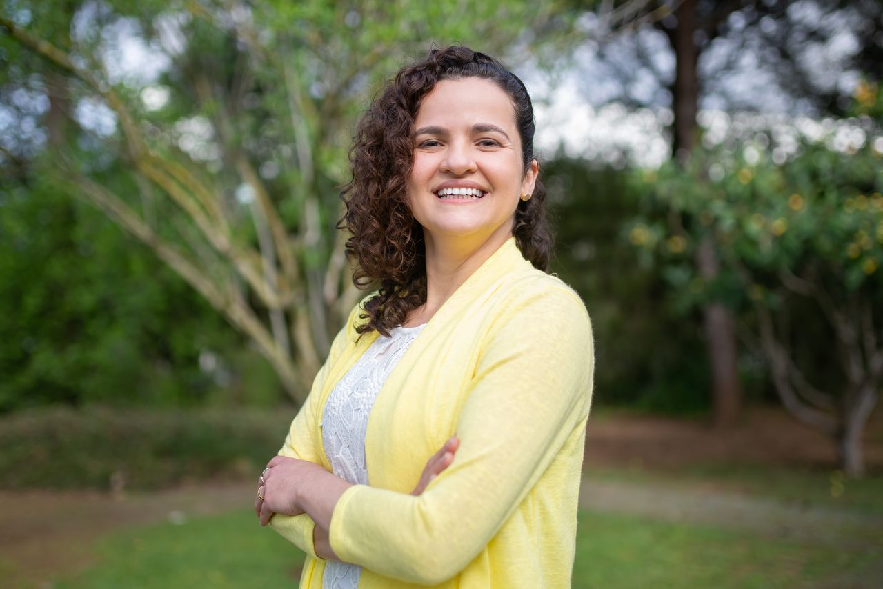 Cheerful woman in a yellow cardigan standing in a lush green garden in Portugal, exuding happiness.